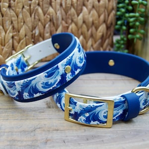 May include: Two dog collars with a blue and white wave pattern. The collars have gold-colored metal buckles and hardware. The collars are made of a combination of white, blue, and gold materials.