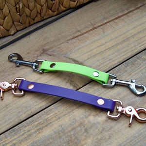 May include: Two leather dog leash attachments with metal clips. One is lime green with a silver clip and the other is purple with a rose gold clip.
