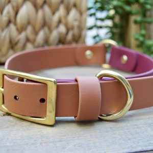 May include: A tan leather dog collar with a gold buckle and D-ring. The collar has a pink underside.