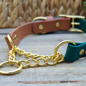 Pu&ograve; includere: Un collare per cani in pelle verde e marrone con una catena dorata e due fibbie dorate. Il collare &egrave; su una superficie di legno.
