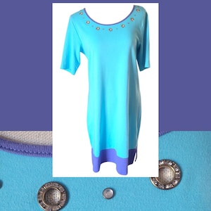 May include: A light blue dress with short sleeves and a scoop neckline. The neckline is trimmed with a purple band and embellished with small, round, silver-colored accents. The hemline features a purple band. The dress is made of a soft, knit fabric.