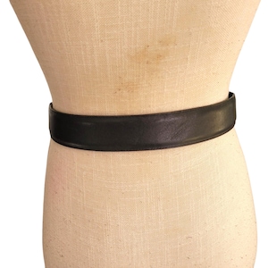 May include: A black leather belt is wrapped around a mannequin. The belt is a solid, dark color and appears to be made of smooth leather. The belt is a simple, classic design.