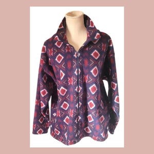 May include: A full-zip fleece jacket in a navy blue hue, adorned with a repeating pattern of red and white geometric shapes. The jacket features a high collar and long sleeves. The fleece material appears soft and comfortable.