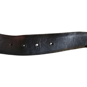 May include: Black leather belt with decorative silver-colored buckle. The belt has three holes and a stitched edge. The buckle has an ornate design. The belt is a classic accessory.