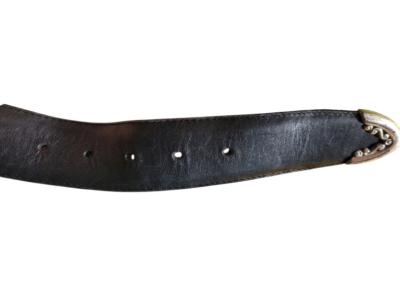 May include: Black leather belt with decorative silver-colored buckle. The belt has three holes and a stitched edge. The buckle has an ornate design. The belt is a classic accessory.