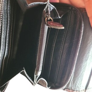 Puede incluir: Cartera de cuero negro abierta con m&uacute;ltiples ranuras para tarjetas y un compartimento con cremallera. La cartera tiene una superficie texturizada y una cremallera met&aacute;lica con un tirador decorativo. El interior es negro.