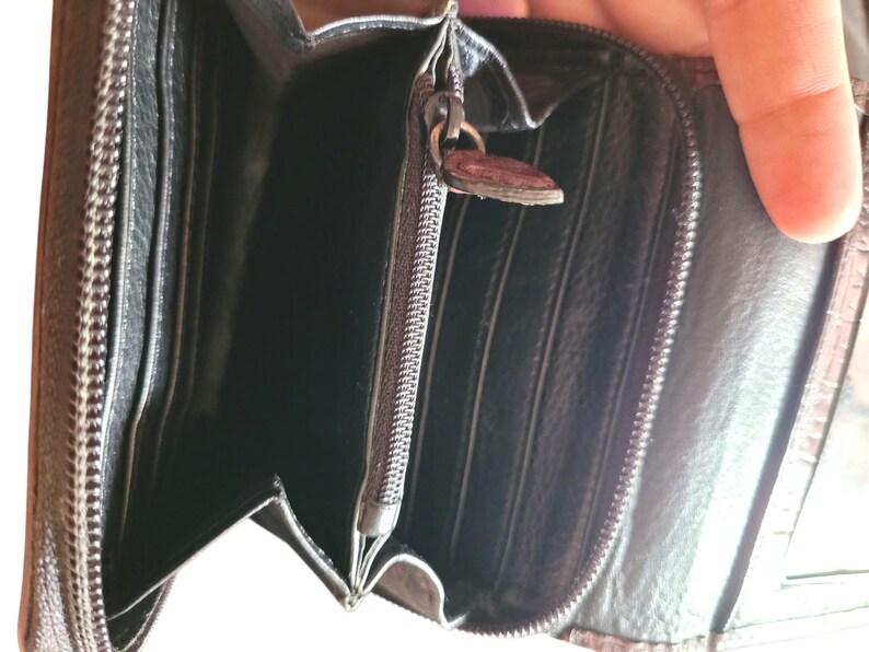 Puede incluir: Cartera de cuero negro abierta con m&uacute;ltiples ranuras para tarjetas y un compartimento con cremallera. La cartera tiene una superficie texturizada y una cremallera met&aacute;lica con un tirador decorativo. El interior es negro.