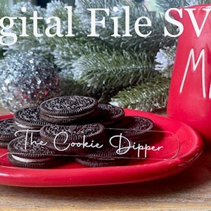 Puede incluir: Una taza de cerámica roja con la palabra "MILK" escrita en blanco en el lateral. Un plato rojo con un cucharón para galletas de plástico transparente y una pila de galletas sándwich de chocolate. El cucharón tiene el texto "The Cookie Dipper" escrito en él.