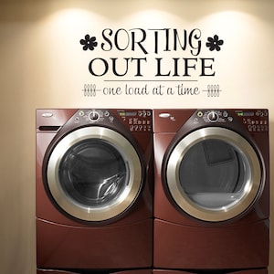 May include: A black and white wall decal with the text "*SORTING* OUT LIFE - one load at a time -" above two brown washing machines.