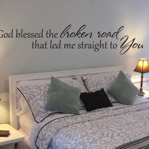 May include: A bedroom with a white bed frame and a white and gray patterned comforter. The wall above the bed has a black vinyl decal with the text "God blessed the broken road that led me straight to You".