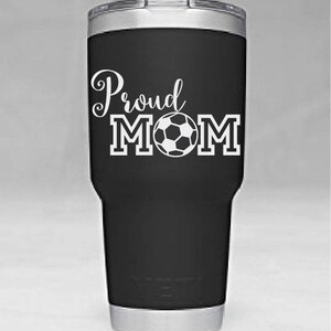 May include: Black stainless steel tumbler with a white design that says "Proud Mom" with a soccer ball in the middle of the word "Mom".