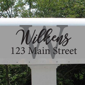 May include: White mailbox with a gray background and black lettering. The mailbox has the name "Wilkens" and the address "123 Main Street" printed on it.