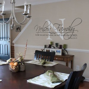 May include: A black and white wall decal with the text "Nelson Family" and a Bible verse, "As for me and my house, we will serve the LORD. Joshua 24:15". The decal is on a beige wall in a dining room with a wooden table and chairs.