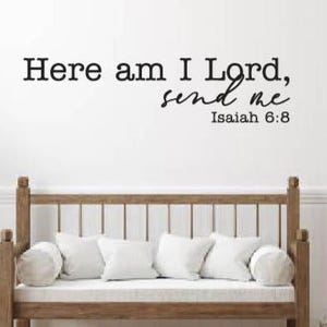 May include: A wooden bench with white cushions and pillows is positioned beneath a wall with the text "Here am I Lord, send me Isaiah 6:8" in black lettering. The bench is in a room with a white wall and a door.