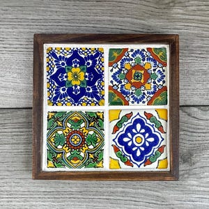 Op de afbeelding: Een houten dienblad met vier kleurrijke keramische tegels met ingewikkelde geometrische patronen in tinten blauw, groen, geel, rood en wit.