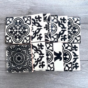 May include: A selection of black and white patterned tiles. The tiles display a range of ornate designs, including floral and geometric motifs. The tiles are arranged on a light grey surface.