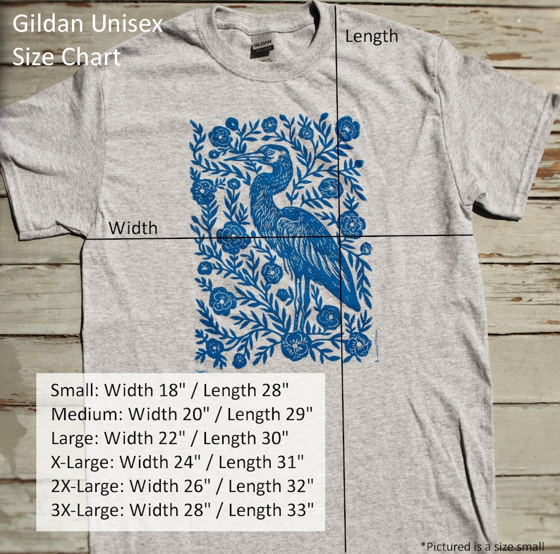 May include: A gray unisex t-shirt with a blue heron and floral print. The size chart shows the width and length measurements for each size: Small (18" x 28"), Medium (20" x 29"), Large (22" x 30"), X-Large (24" x 31"), 2X-Large (26" x 32"), and 3X-Large (28" x 33").