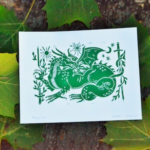 Puede incluir: Grabado en linóleo verde de un dragón con las alas extendidas, rodeado de estrellas y una luna creciente. La impresión está firmada "Dragon Lore" y "Jatavian Truett 2017".