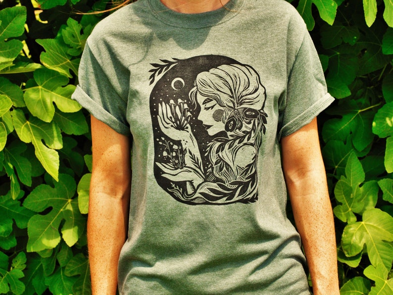 May include: A green t-shirt with a black and white illustration of a woman with flowers and a crescent moon.