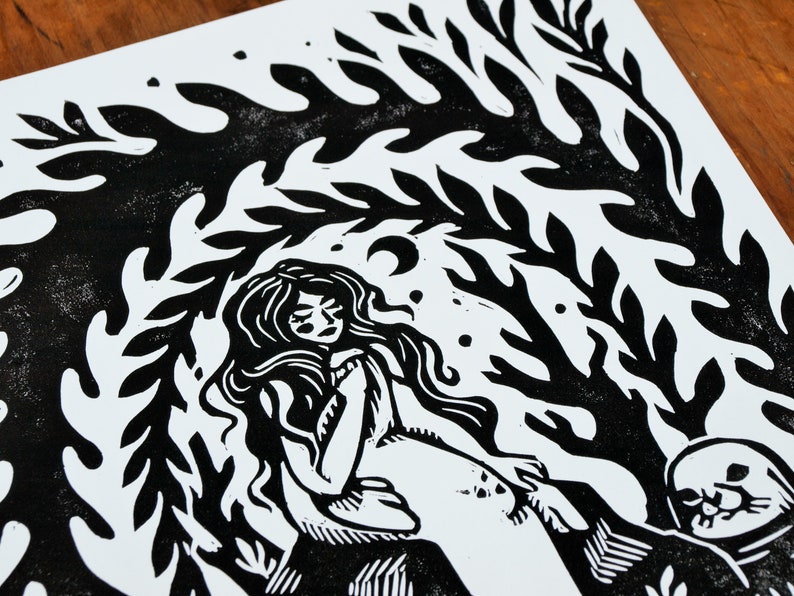 May include: Black and white linocut print of a woman with long hair sitting under a leafy canopy. The woman is wearing a simple dress and has her eyes closed. A small animal is sitting beside her.