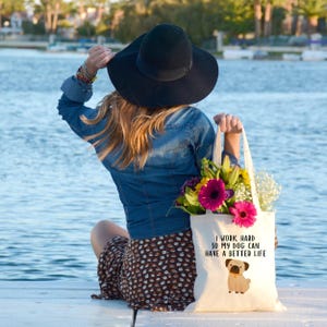 Woman carrying the pug dog tote filled with flowers while seated beside a lake.