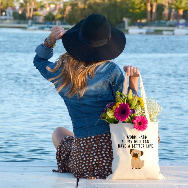 Woman carrying the pug dog tote filled with flowers while seated beside a lake.