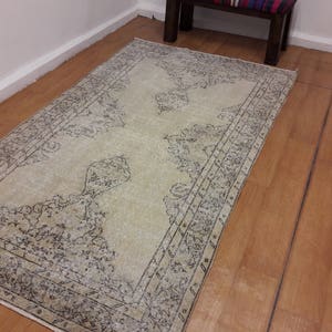 May include: A vintage cream-colored rug with a black and gray floral pattern. The rug has a distressed look and is perfect for adding a touch of bohemian style to any room.