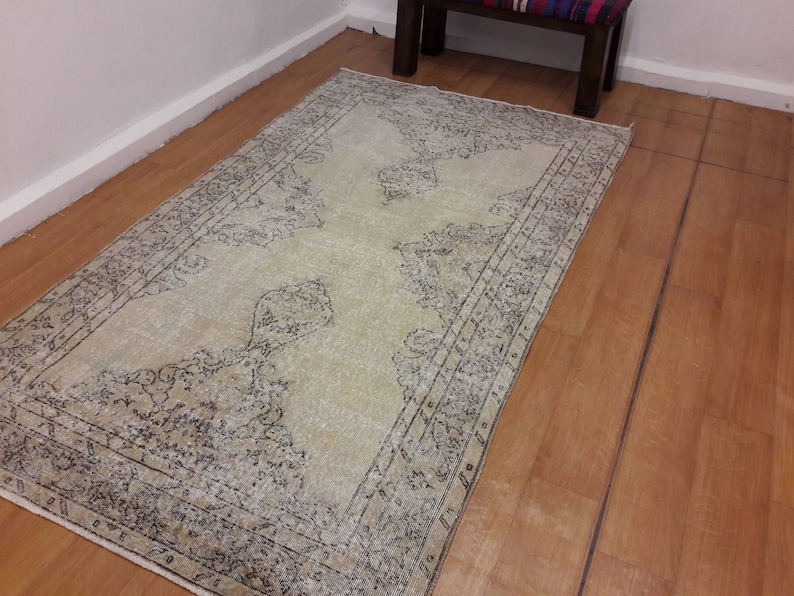 May include: A vintage cream-colored rug with a black and gray floral pattern. The rug has a distressed look and is perfect for adding a touch of bohemian style to any room.