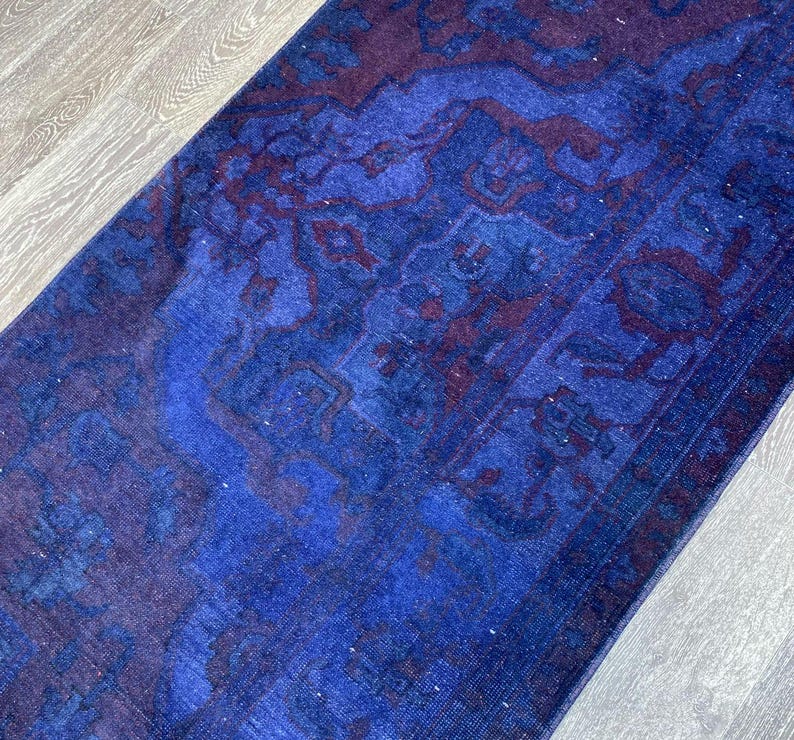 Pu&ograve; includere: Un tappeto vintage blu e viola con un motivo floreale sbiadito. Il tappeto ha un aspetto usurato ed &egrave; realizzato in un materiale morbido e tessuto.