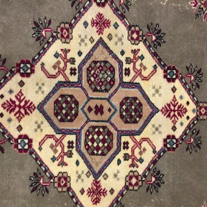 May include: A beige rug with a central diamond-shaped design featuring intricate geometric patterns in shades of red, blue, and brown. The rug has a faded, vintage look.