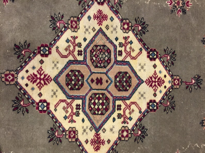 May include: A beige rug with a central diamond-shaped design featuring intricate geometric patterns in shades of red, blue, and brown. The rug has a faded, vintage look.