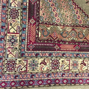 May include: Close-up of a colorful rug with intricate patterns in shades of blue, red, and beige. The rug has a traditional design with geometric shapes and floral motifs.