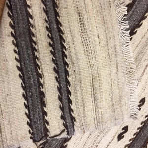 May include: Close-up of a white and brown woven rug with a geometric pattern. The rug has a fringe on one side.