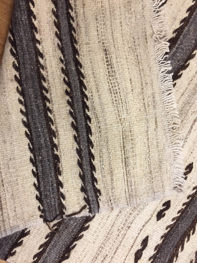 May include: Close-up of a white and brown woven rug with a geometric pattern. The rug has a fringe on one side.