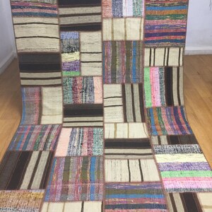 Op de afbeelding: Een patchwork tapijt met een verscheidenheid aan kleuren en patronen, waaronder bruin, wit, roze, blauw en groen. Het tapijt is gemaakt van geweven stof en heeft een rustieke, handgemaakte uitstraling.