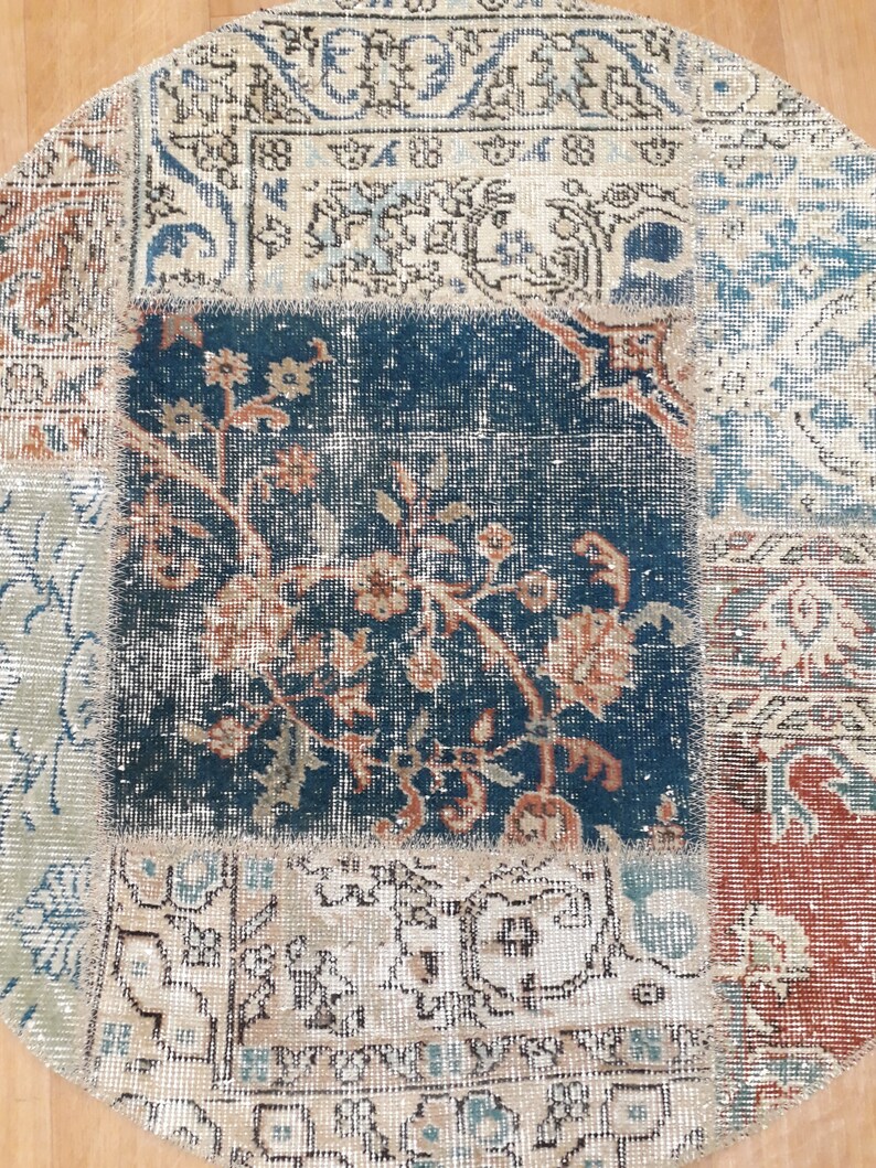 May include: A round patchwork rug with a variety of colors and patterns, including blue, beige, and red. The rug is made of different pieces of fabric sewn together.