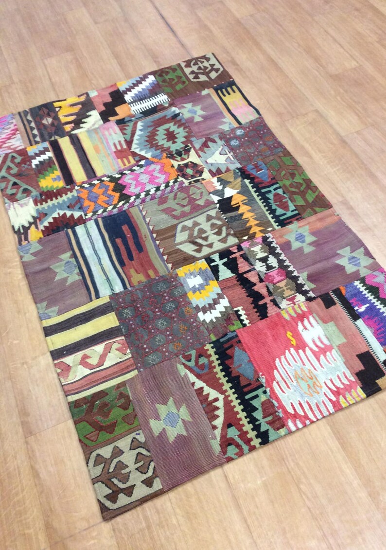 May include: A colorful patchwork rug with a variety of geometric patterns in shades of red, blue, green, yellow, and brown. The rug is made of woven fabric and has a fringed edge.
