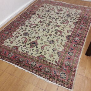 May include: A cream-colored rug with a floral pattern in shades of pink, green, and blue. The rug has a fringed edge and a border with a repeating pattern.