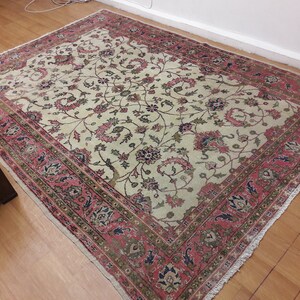 May include: A vintage cream-colored rug with a floral pattern in shades of pink, green, and blue. The rug has a fringed border and is in good condition.