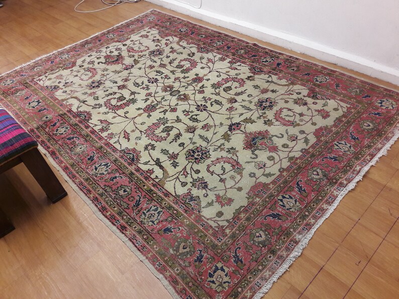 May include: A vintage cream-colored rug with a floral pattern in shades of pink, green, and blue. The rug has a fringed border and is in good condition.