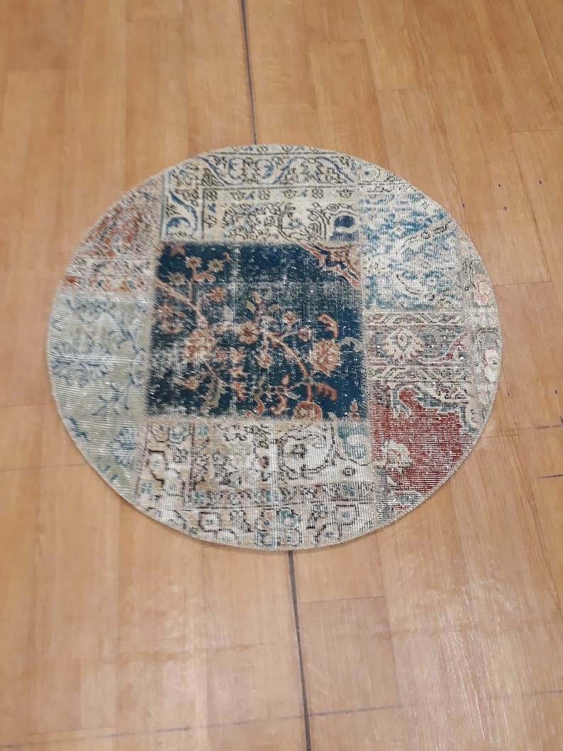 May include: A round, multi-colored rug with a patchwork design. The rug has a cream background with blue, red, and green accents. The rug is made of woven fabric and has a fringed edge.