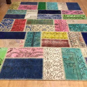 Op de afbeelding: Een kleurrijk patchwork tapijt gemaakt van verschillende stukken stof. Het tapijt is gemaakt van verschillende kleuren, waaronder blauw, groen, roze, geel en rood. Het tapijt heeft een unieke en eclectische stijl.
