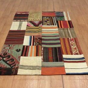 Puede incluir: Una alfombra de retazos multicolor con una variedad de patrones. La alfombra está hecha de piezas de tela rectangulares y cuadradas cosidas. Los colores incluyen rojo, azul, verde, naranja y beige. La alfombra está sobre un suelo de madera.