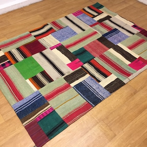 Könnte beinhalten: Ein Patchwork-Teppich aus verschiedenen farbigen Stoffen mit Streifen und Mustern. Der Teppich besteht aus vielen Quadraten und Rechtecken, und die Farben sind hell und lebendig.