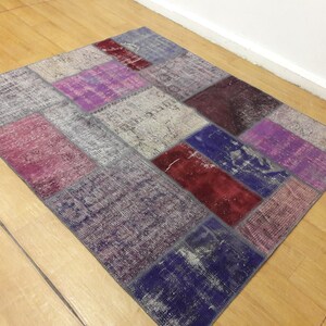 May include: A patchwork rug with a variety of colors and patterns, including purple, pink, red, and blue. The rug is made of woven fabric and has a distressed look.