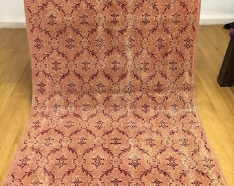 Könnte beinhalten: Ein Vintage-Teppich mit einem sich wiederholenden geometrischen Muster in Rot- und Cremetönen. Der Teppich hat einen abgenutzten Look und ist aus einem weichen, gewebten Material gefertigt.