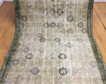 May include: A vintage rug with a faded floral pattern in shades of brown, green, and white. The rug has a green border and is made of a woven material.