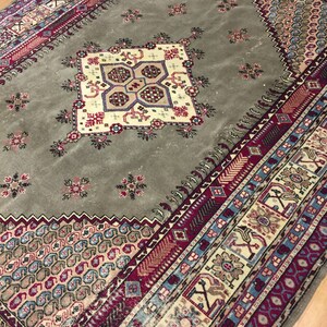 May include: A vintage rug with a muted green background and a central medallion with intricate floral and geometric patterns. The rug has a border with a repeating pattern of red, blue, and white.