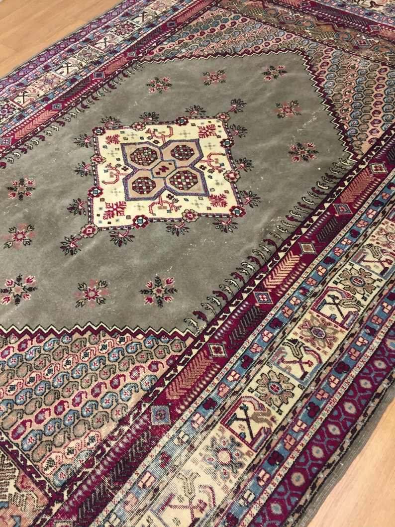 May include: A vintage rug with a muted green background and a central medallion with intricate floral and geometric patterns. The rug has a border with a repeating pattern of red, blue, and white.