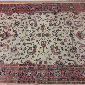 May include: A vintage cream-colored rug with a floral pattern in shades of pink, green, and blue. The rug has a border with a repeating pattern of pink, green, and blue.